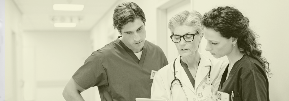 Paramedic Practitioner and healthcare professionals reviewing patient information on a tablet in a GP Surgery corridor, highlighting teamwork and collaboration in primary care. Vela Medical Group connects paramedic practitioners with top locum and permanent roles across the UK.